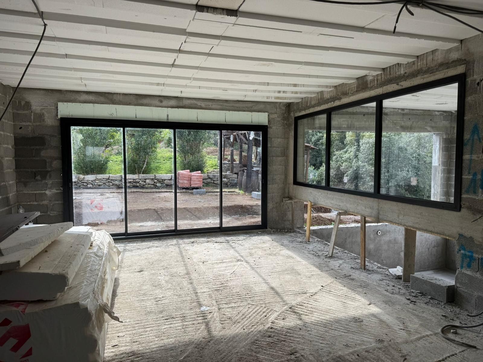 Intérieur d'une maison moderne avec de grandes portes coulissantes en verre s'ouvrant sur un jardin verdoyant.