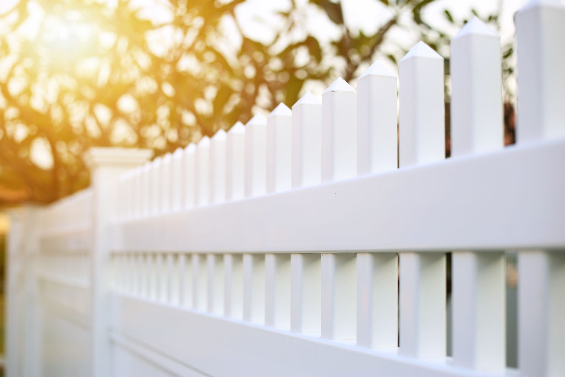 Clôture blanche sous un soleil chaud, avec des arbres dorés flous en arrière-plan.