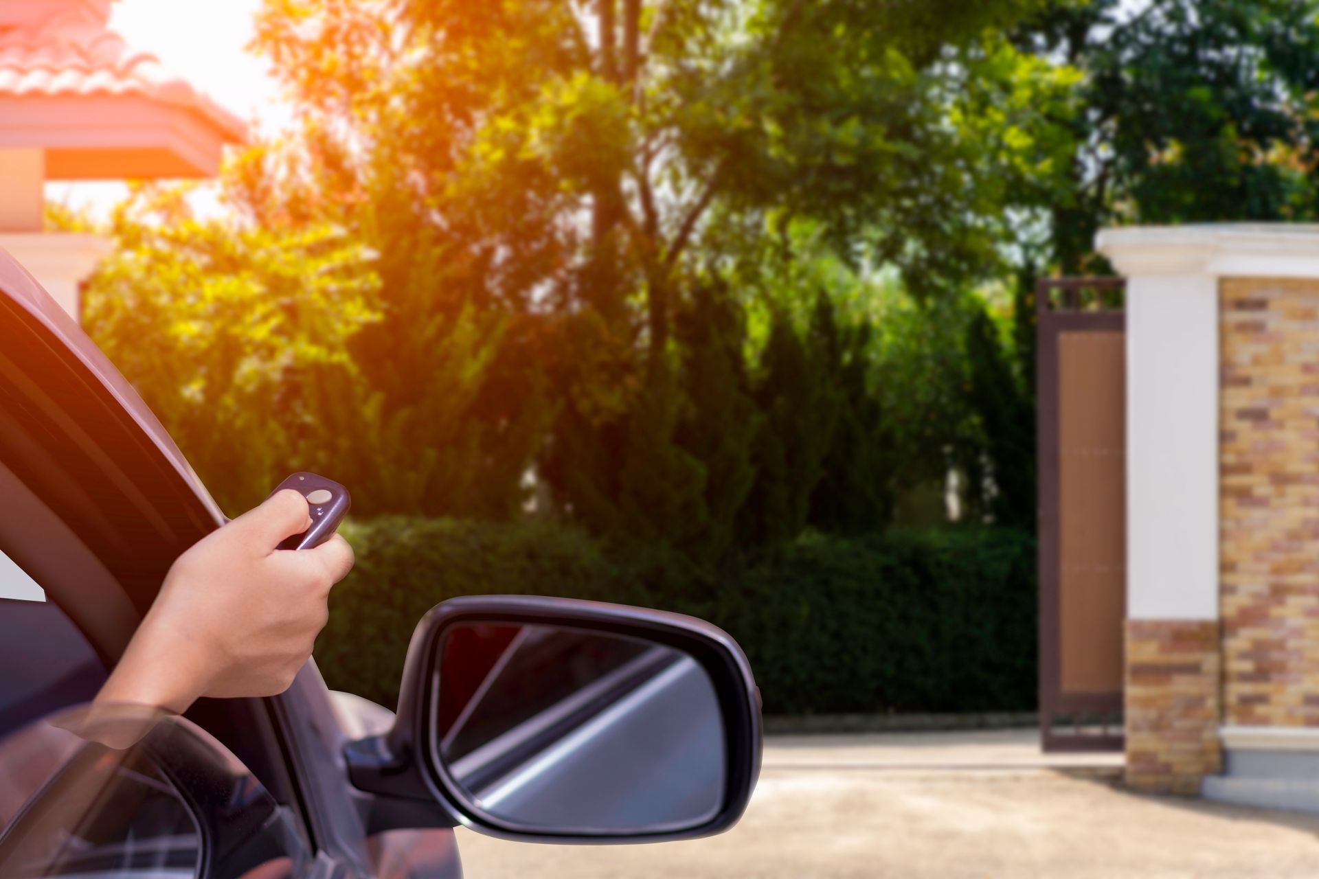 Une main tenant une clé de voiture à côté d'un rétroviseur, dans une allée ensoleillée.