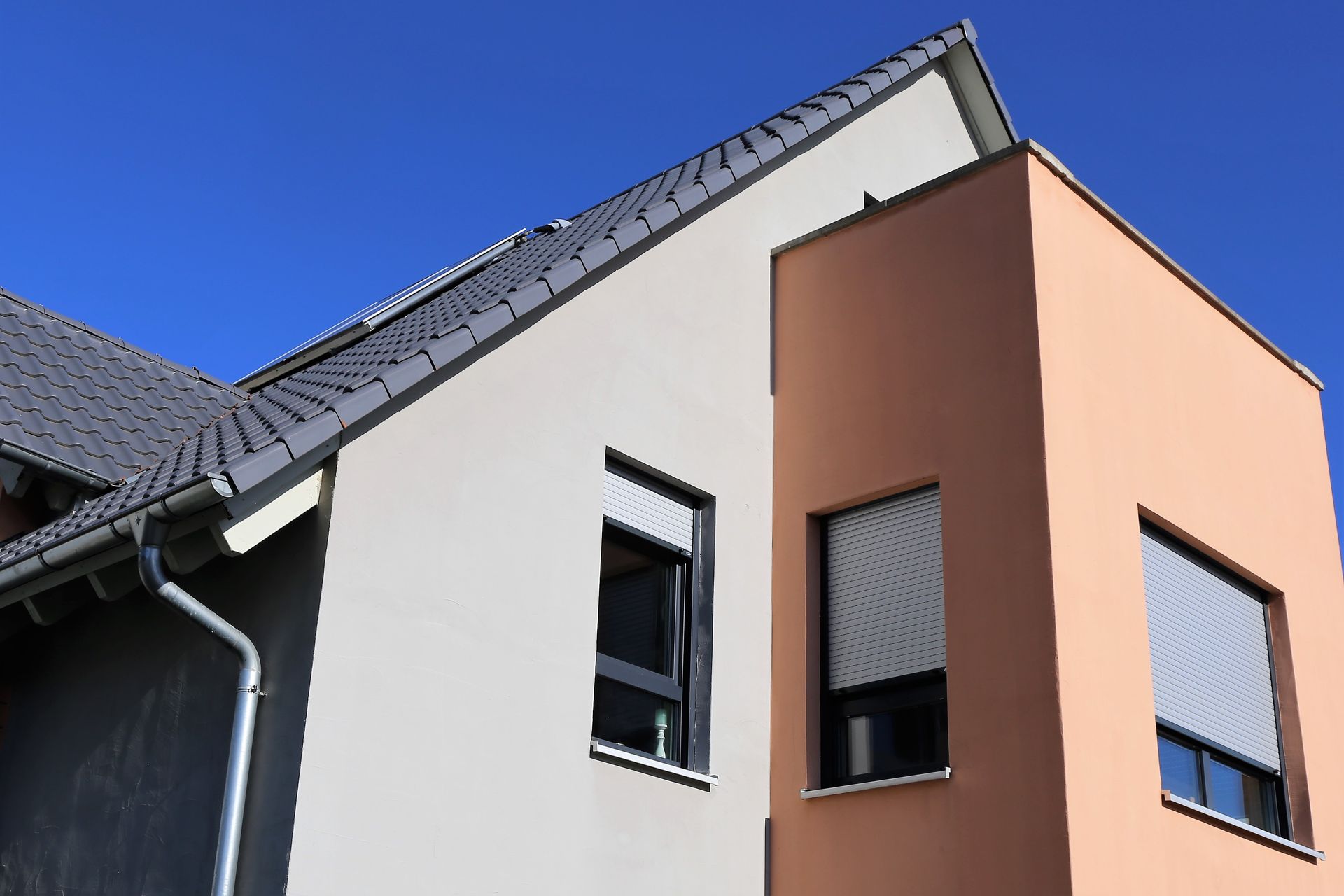 Coin d'une maison moderne aux murs blancs et pêche, toit foncé et deux fenêtres.