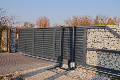 Portail coulissant en métal noir à côté d'un mur de pierre à l'entrée d'une allée.