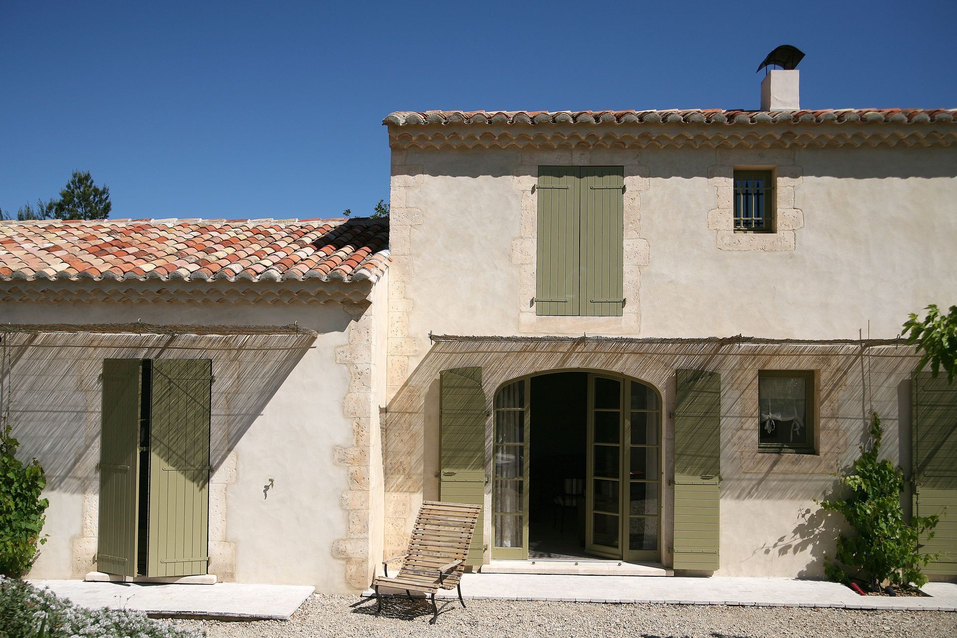 Maison rustique en pierre blanche avec des volets verts et un toit de tuiles sous un ciel bleu clair.