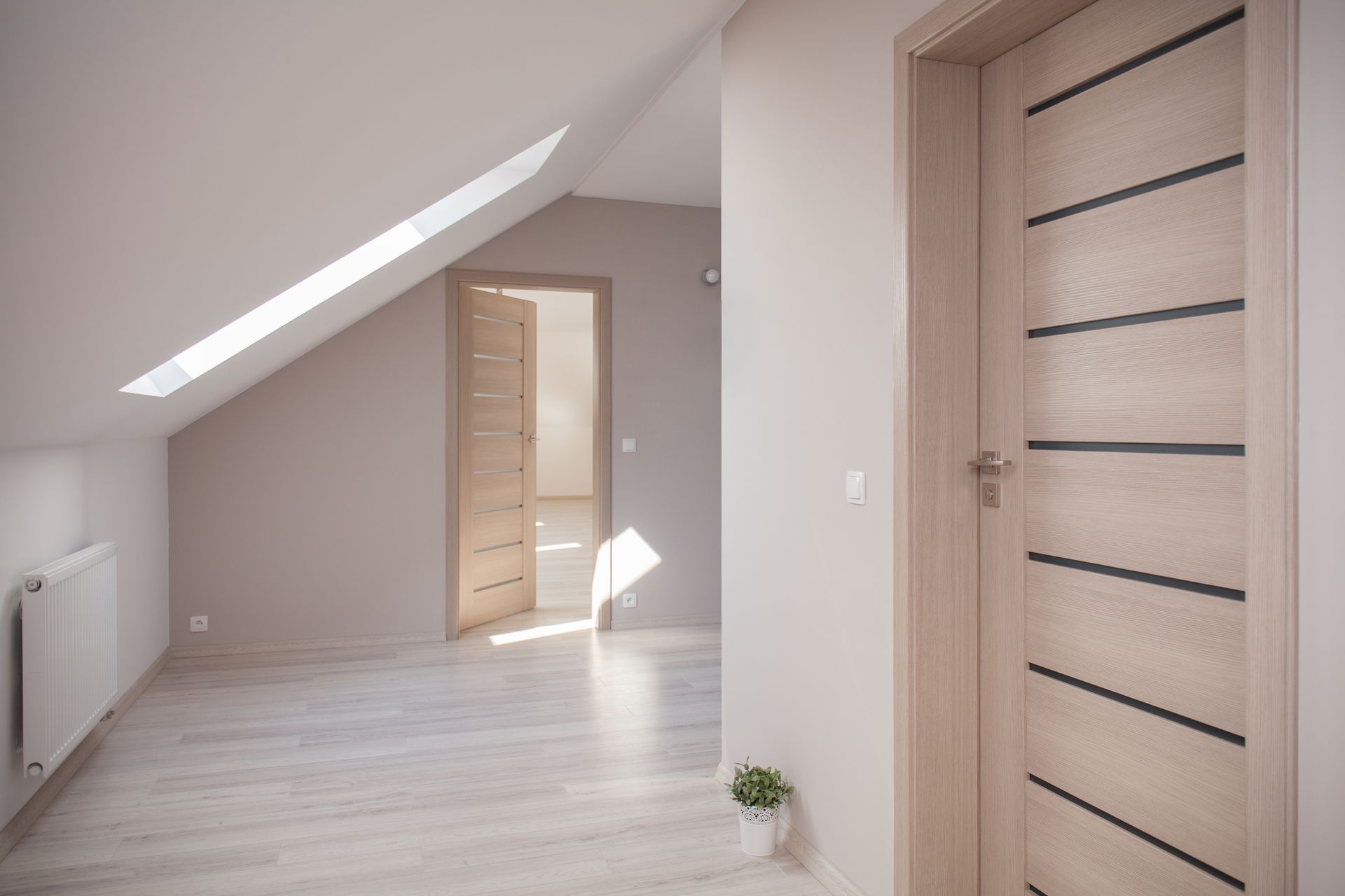 Couloir lumineux et vide sous les combles, avec puits de lumière incliné, portes en bois clair et sol clair.