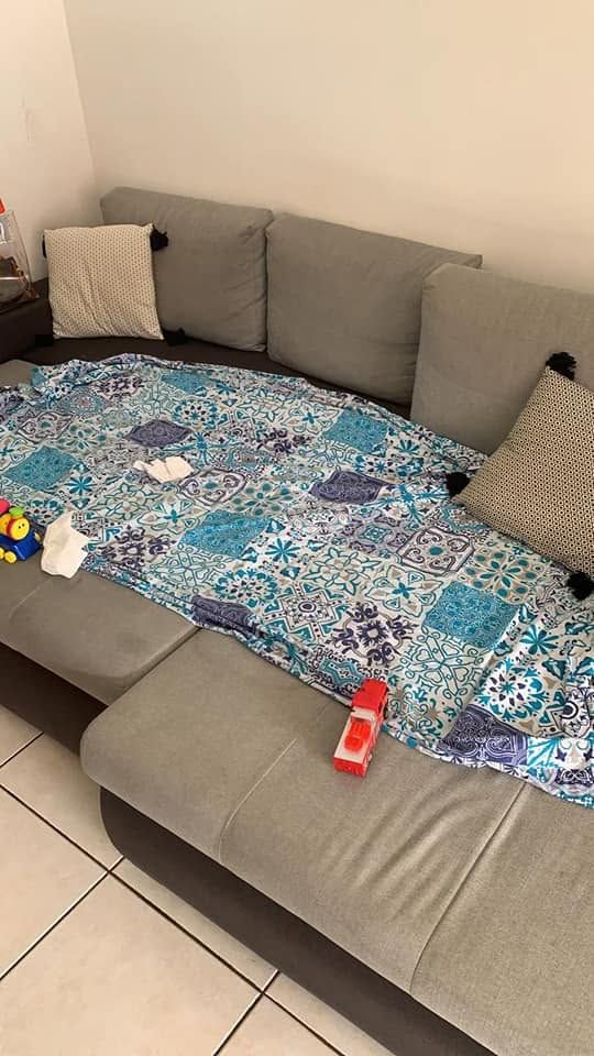 Canapé d'angle gris avec housse bleue à motifs, coussins et quelques objets épars dans un salon