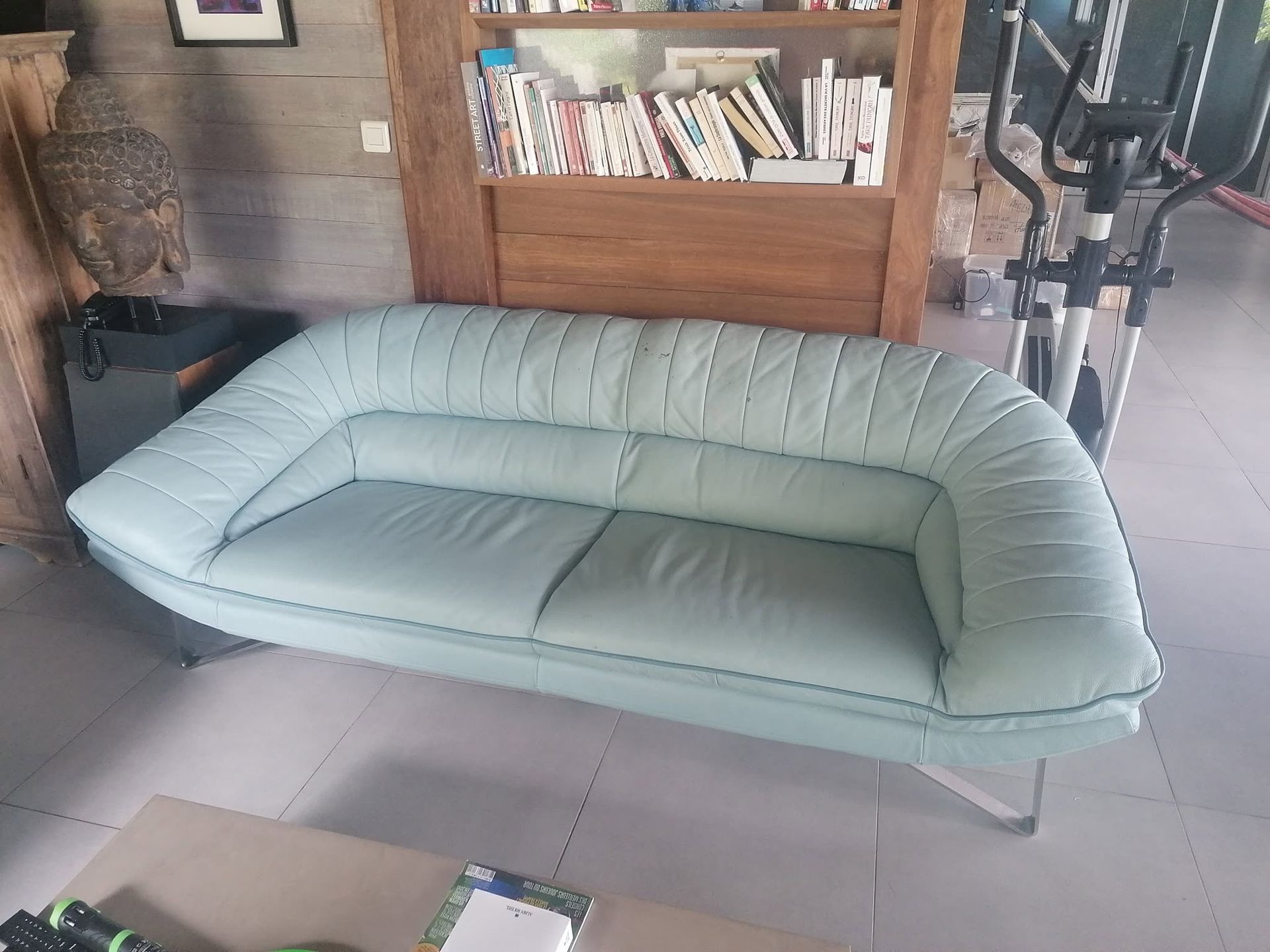 Canapé gonflable bleu clair dans une pièce avec sol carrelé et bibliothèque en arrière-plan