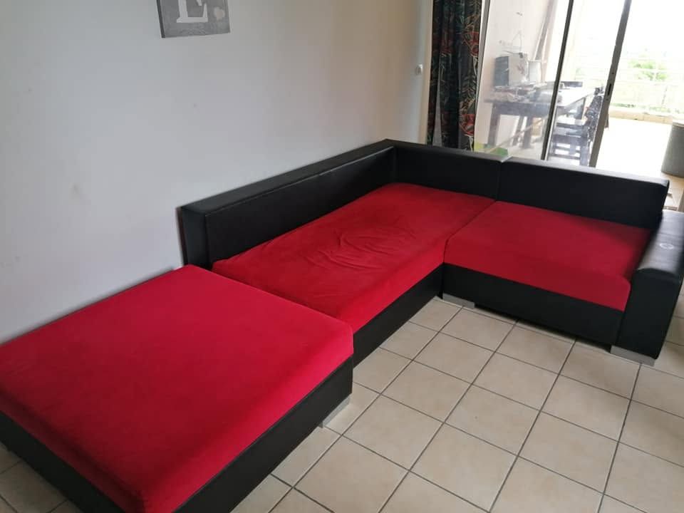 Canapé d'angle en L rouge et noir dans une pièce carrelée lumineuse, avec un pouf assorti.