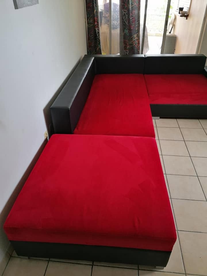 Canapé d'angle rouge et noir dans une pièce intérieure carrelée, près d'un couloir.