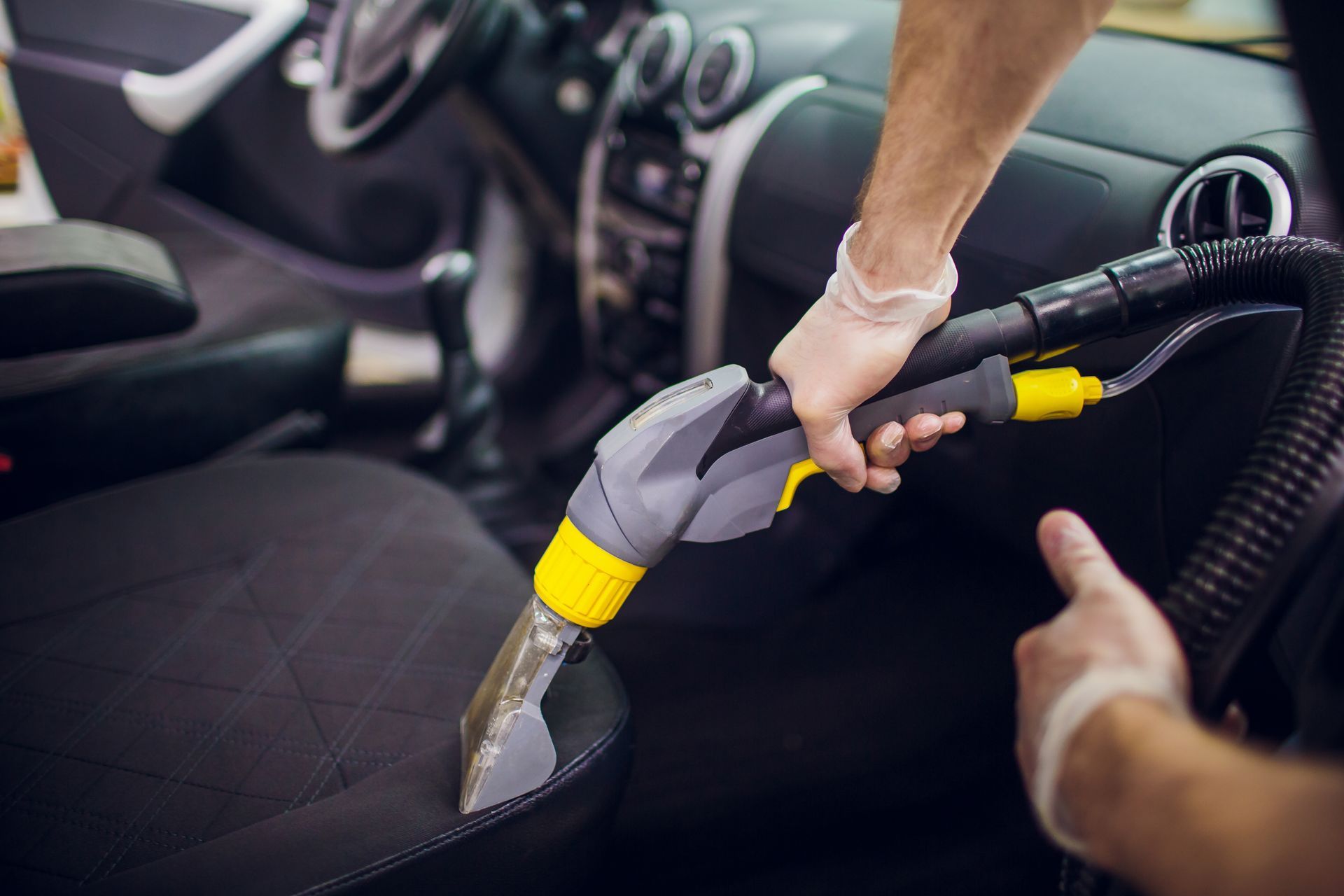 Main utilisant un embout d'aspirateur pour nettoyer l'intérieur d'un siège de voiture