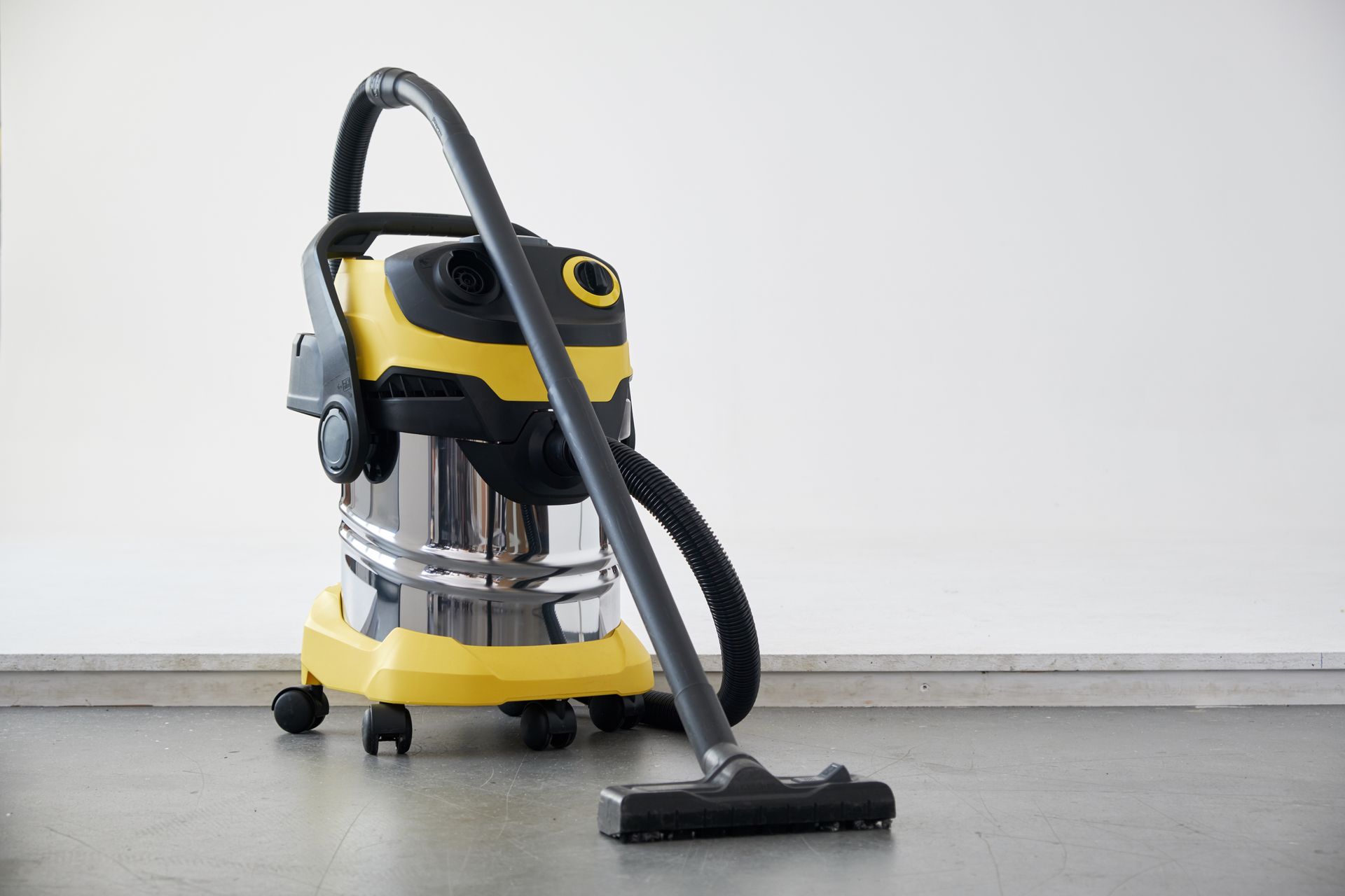 Aspirateur d'atelier jaune et noir avec tuyau et embout pour sols sur un sol gris