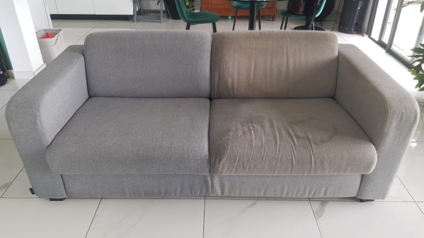 Canapé deux places gris avec un coussin beige usé dans une pièce intérieure lumineuse