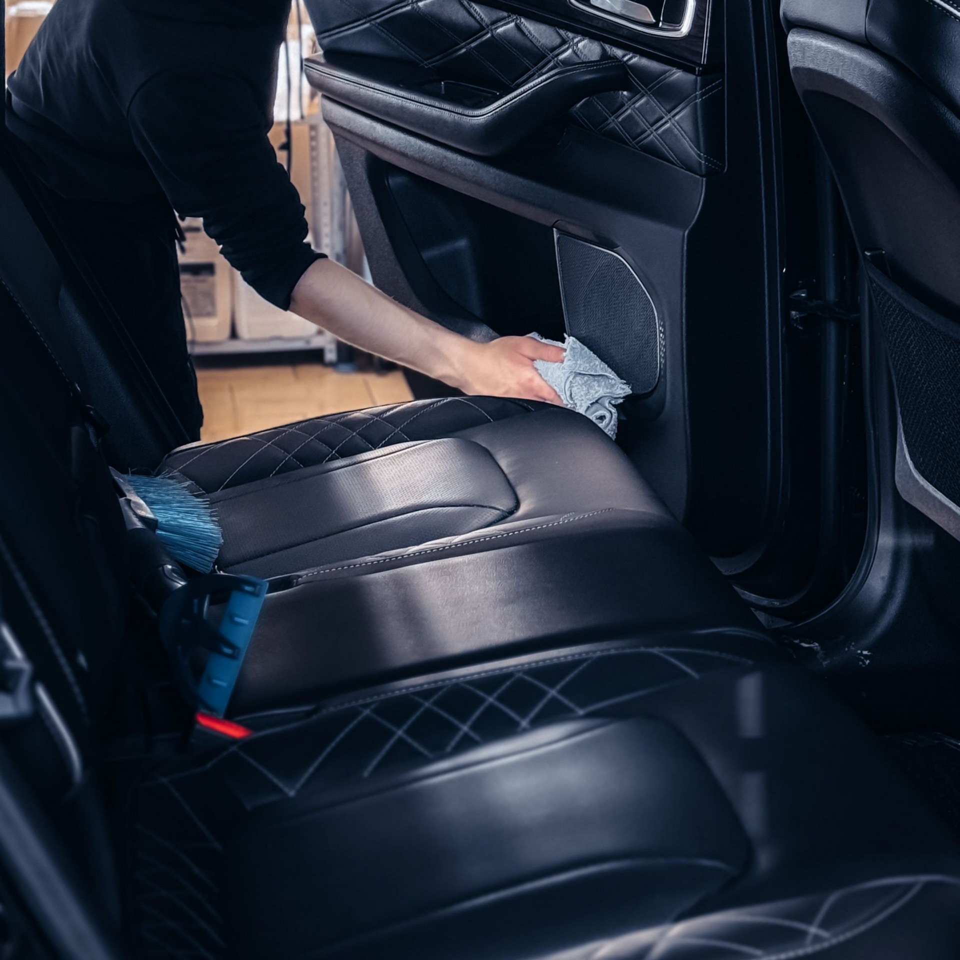 Une personne nettoie l'intérieur en cuir noir d'une voiture de luxe avec un chiffon.