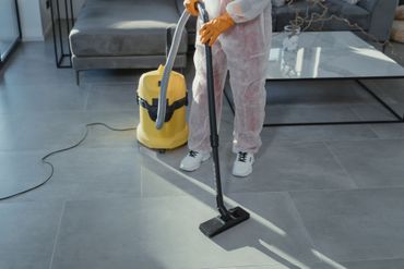 Une personne passe l'aspirateur sur un sol gris dans un salon moderne avec un aspirateur traîneau jaune.