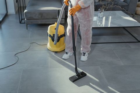 Une personne passe l'aspirateur sur un sol gris dans un salon moderne avec un aspirateur traîneau jaune.