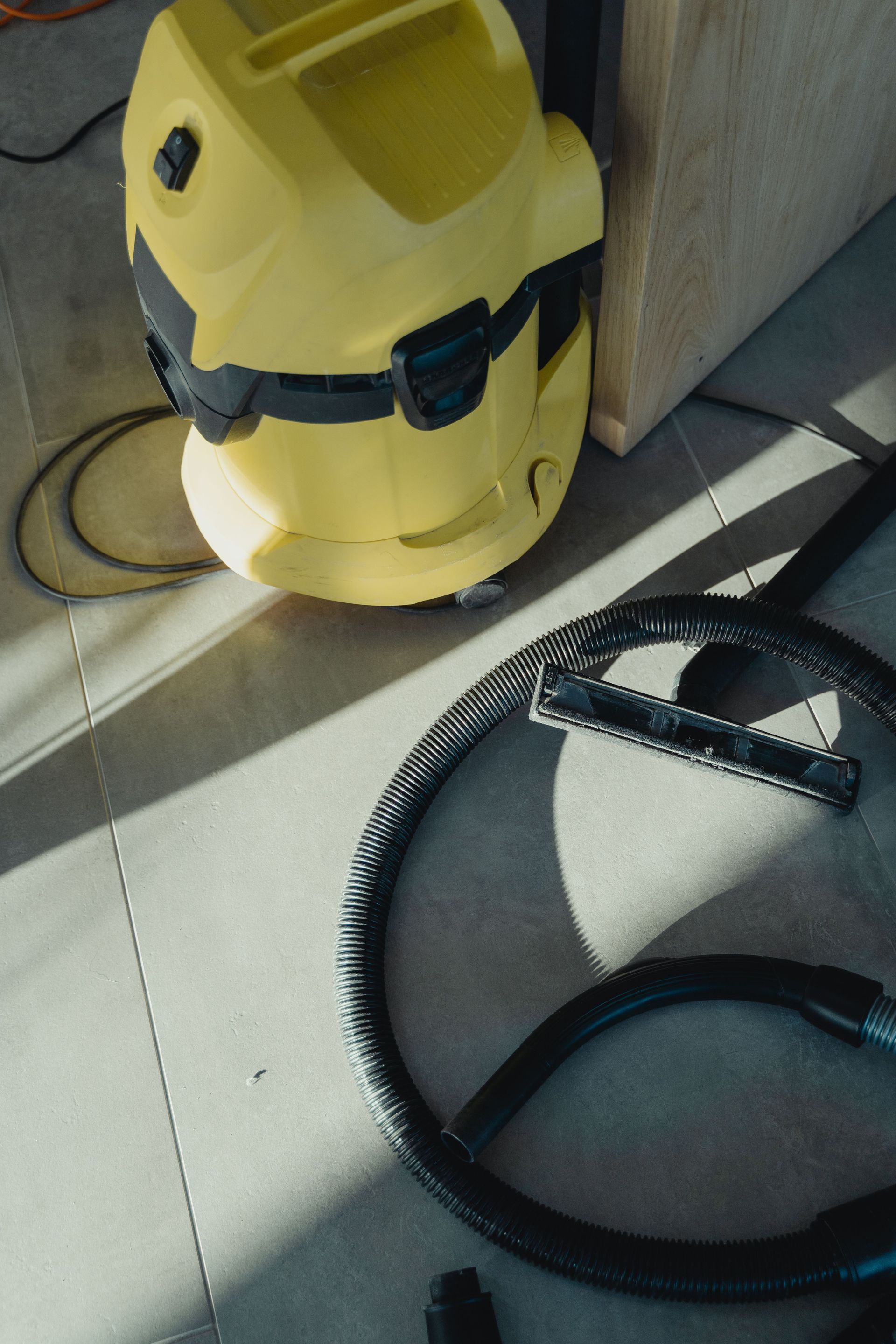 Aspirateur eau et poussière jaune avec tuyau noir sur un sol carrelé au soleil.