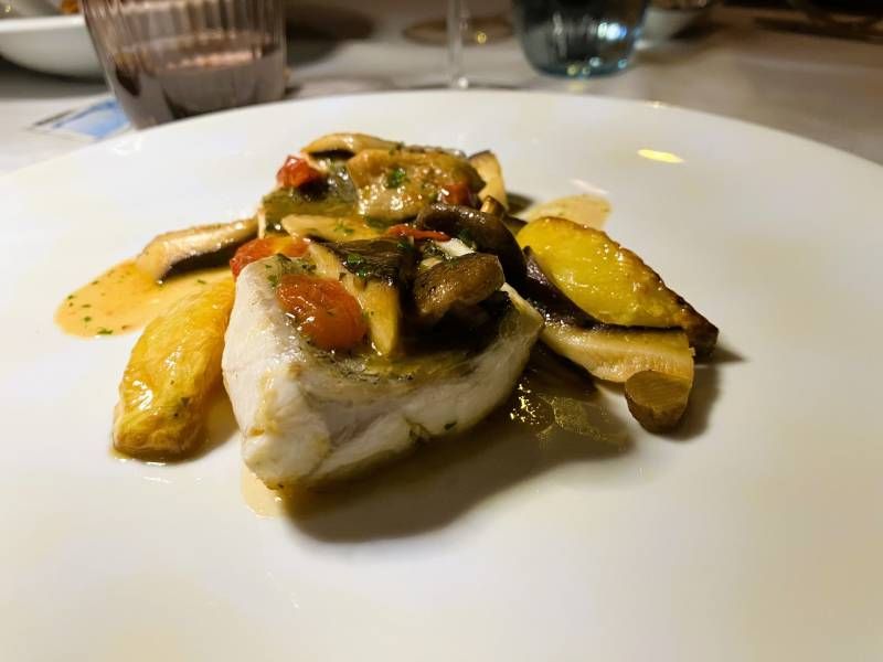 Une assiette blanche surmontée d'un morceau de poisson et de légumes.