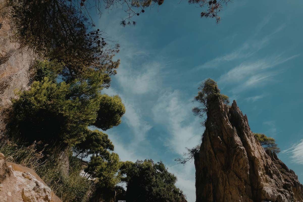 Acantilado rocoso y árboles frondosos bajo un cielo azul con nubes tenues