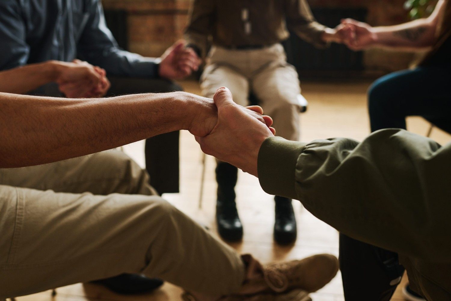 Personas sentadas en círculo tomadas de la mano durante una discusión grupal o una sesión de apoyo.