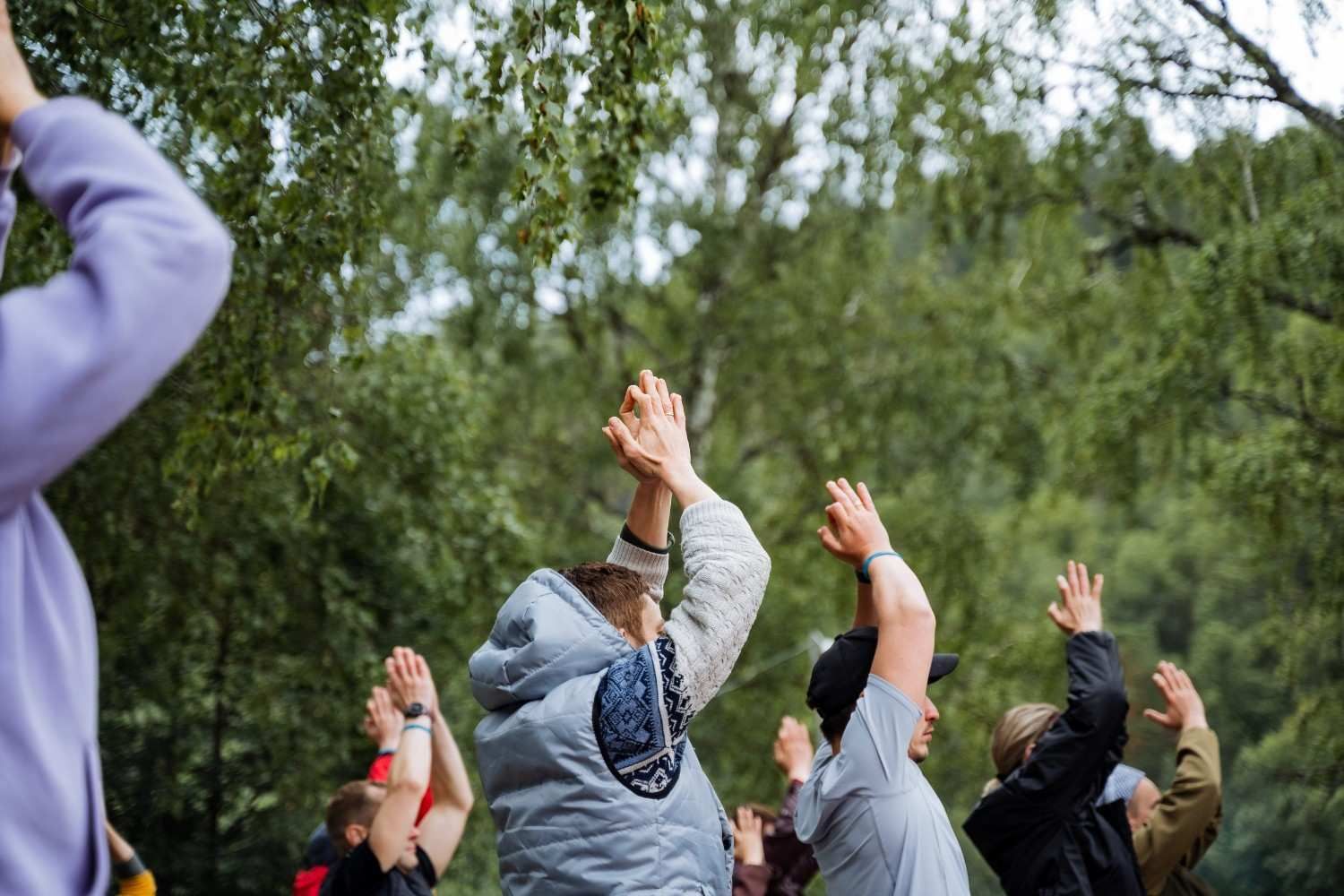 Personas al aire libre con los brazos en alto en una sesión de ejercicio o estiramiento en grupo cerca de árboles.