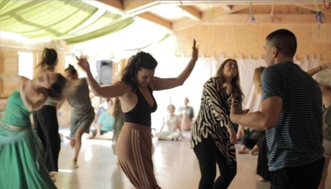 Un grupo de personas sentadas en círculo sobre esterillas de yoga en un estudio luminoso escuchan durante una clase de meditación.