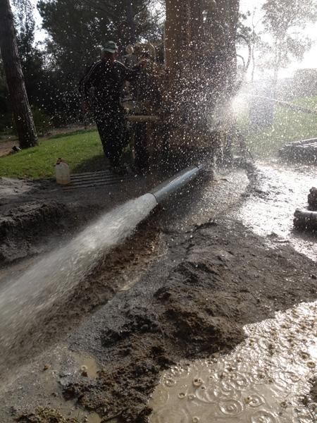 Un hombre está usando una manguera para rociar agua sobre un suelo fangoso.