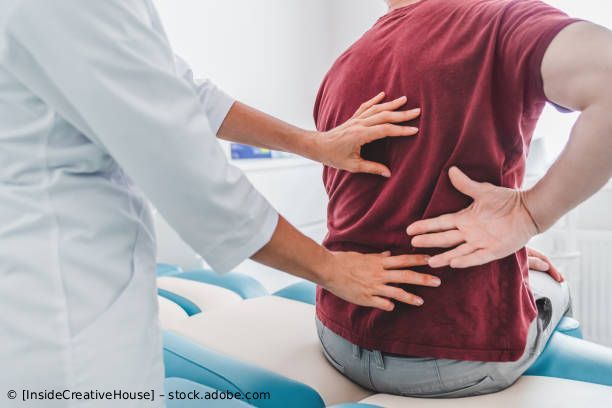 Ein Physiotherapeut stützt eine Person mit Rückenschmerzen auf einer Behandlungsliege.