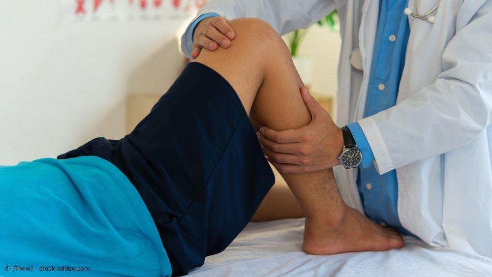 Ein Arzt untersucht das angewinkelte Bein eines Patienten auf einem Untersuchungstisch.