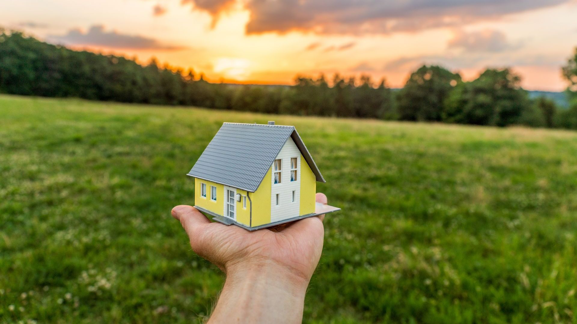 Figurine de maison dans une mains dans un champ