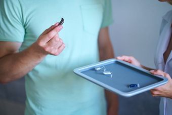 Ein Mann hält ein Paar Hörgeräte, während eine Frau ein Tablett mit Hörgeräten hält. Ein Mann hält ein Paar Hörgeräte, während eine Frau ein Tablett mit Hörgeräten hält