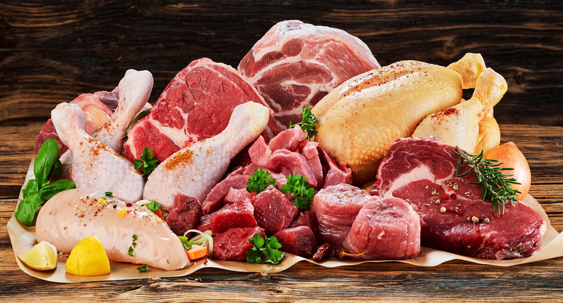 Assortiment de viandes crues et de volailles coupées sur une planche en bois, comprenant du poulet, du porc et du bœuf.