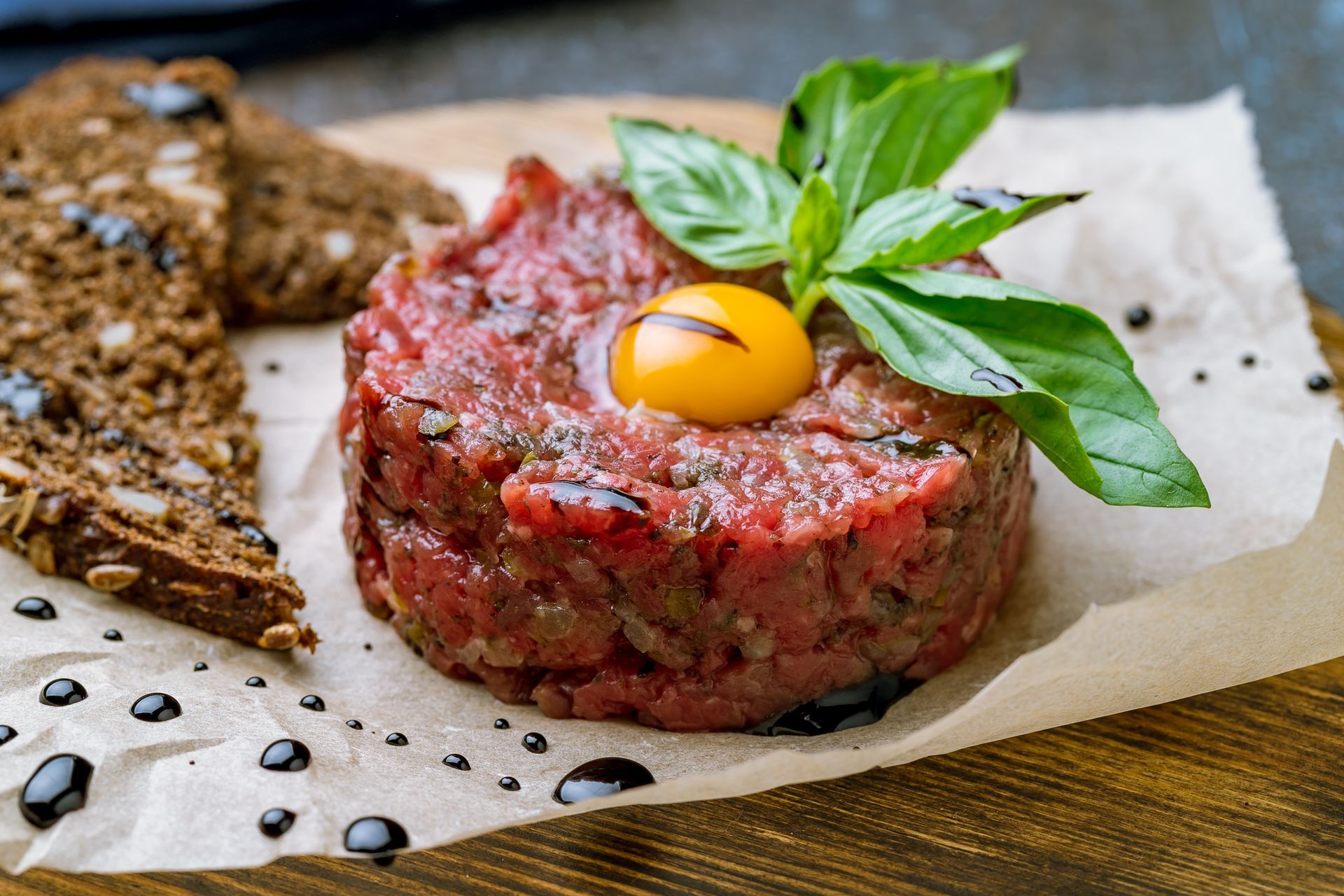 Tartare de bœuf cru garni d'un jaune d'œuf et de basilic, servi sur du papier sulfurisé avec du pain grillé