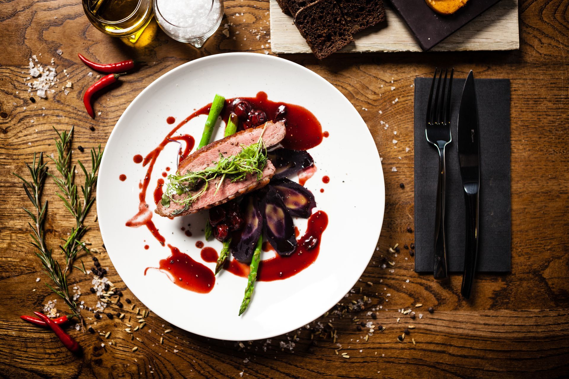 Viande dressée avec haricots verts et sauce tomate sur une table rustique en bois, avec les couverts à côté.