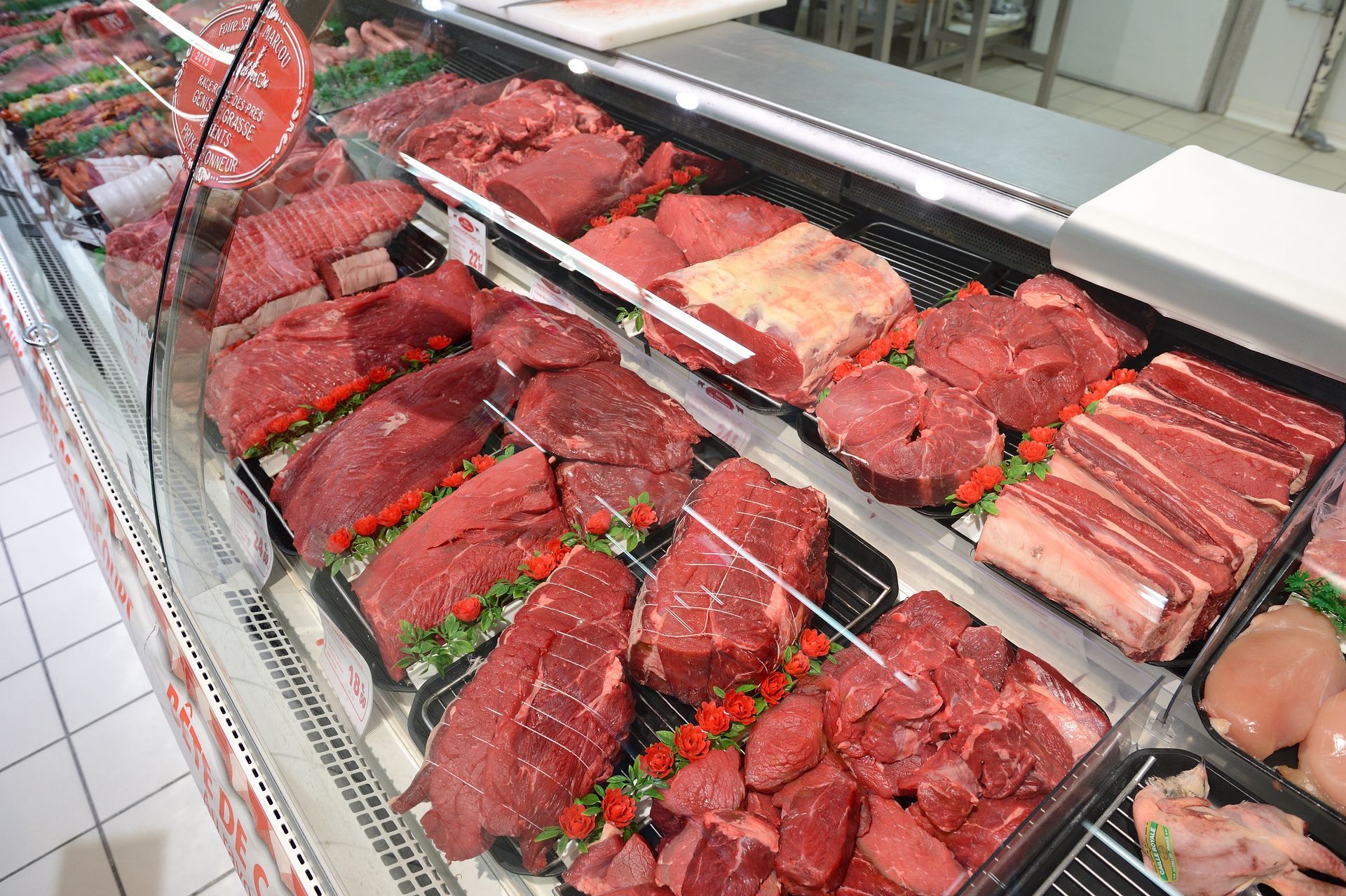 Vitrine présentant un assortiment de viandes crues dans une épicerie, avec des plateaux de steaks, de côtes et de viande hachée.