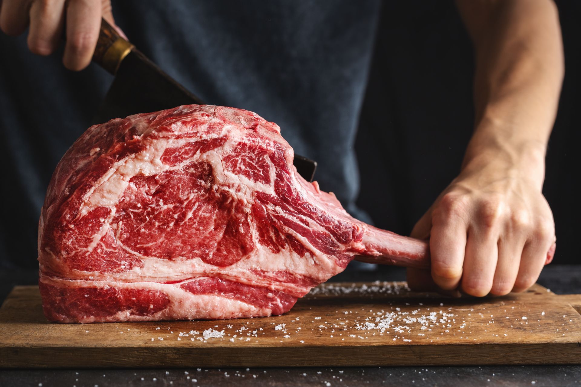 Des mains découpant un steak persillé cru sur une planche à découper en bois
