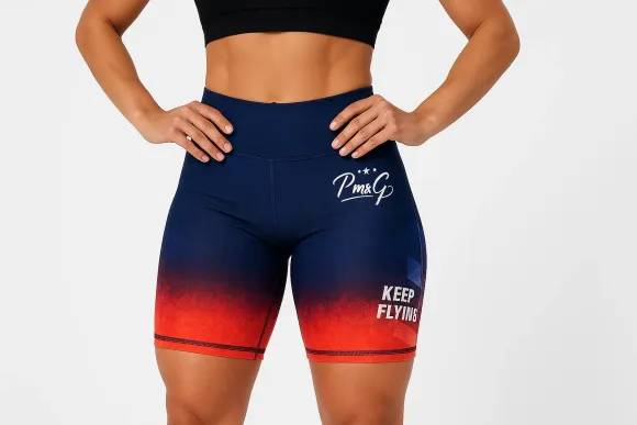 Mujer con shorts azul marino y rojo degradado y top corto negro, con las manos en las caderas. Texto