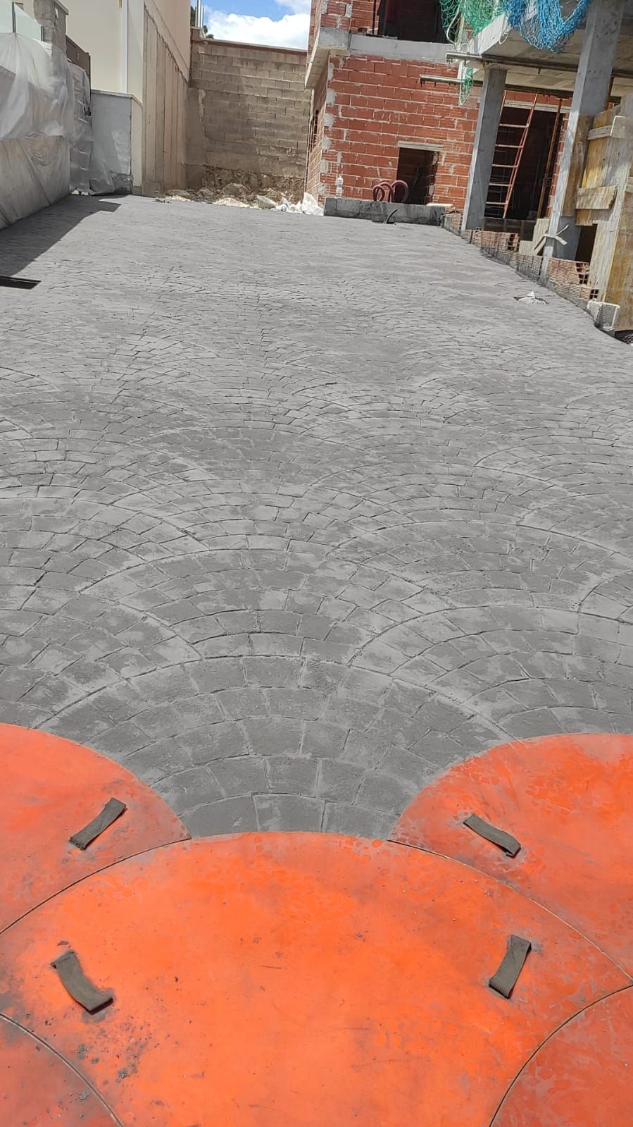 Patio cubierto de grava con muros de ladrillo sin terminar y piezas de maquinaria de color naranja en primer plano.