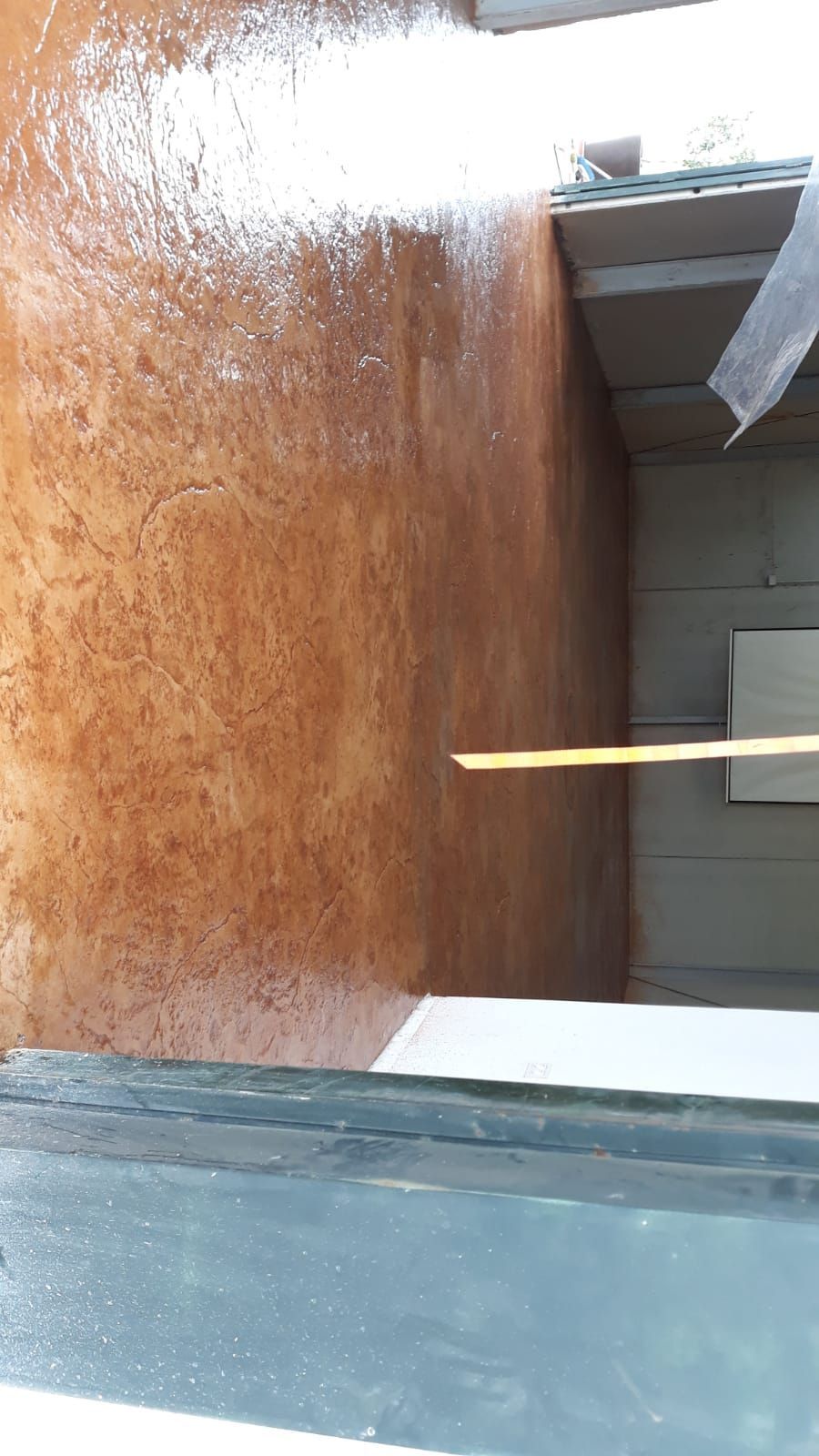 Terraza de madera mojada con barandilla blanca y puerta de cristal, vista desde el interior.