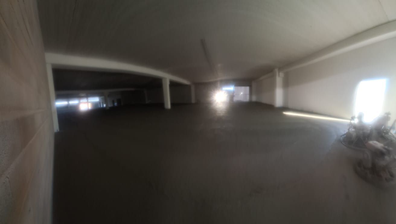 Un aparcamiento subterráneo con poca luz, pilares de hormigón y luces brillantes al fondo.
