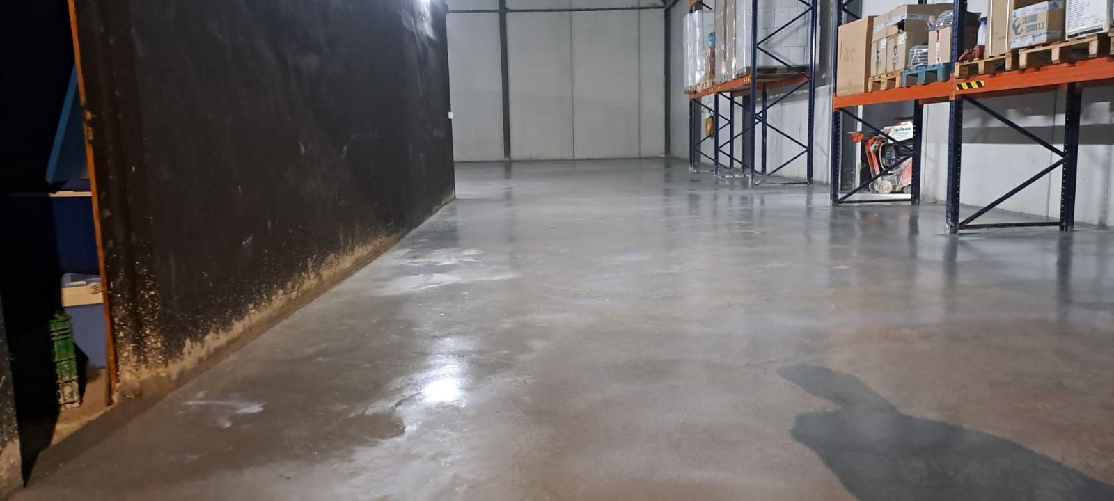 Pasillo vacío de almacén con suelo de hormigón pulido y estanterías de almacenamiento a lo largo de los laterales.