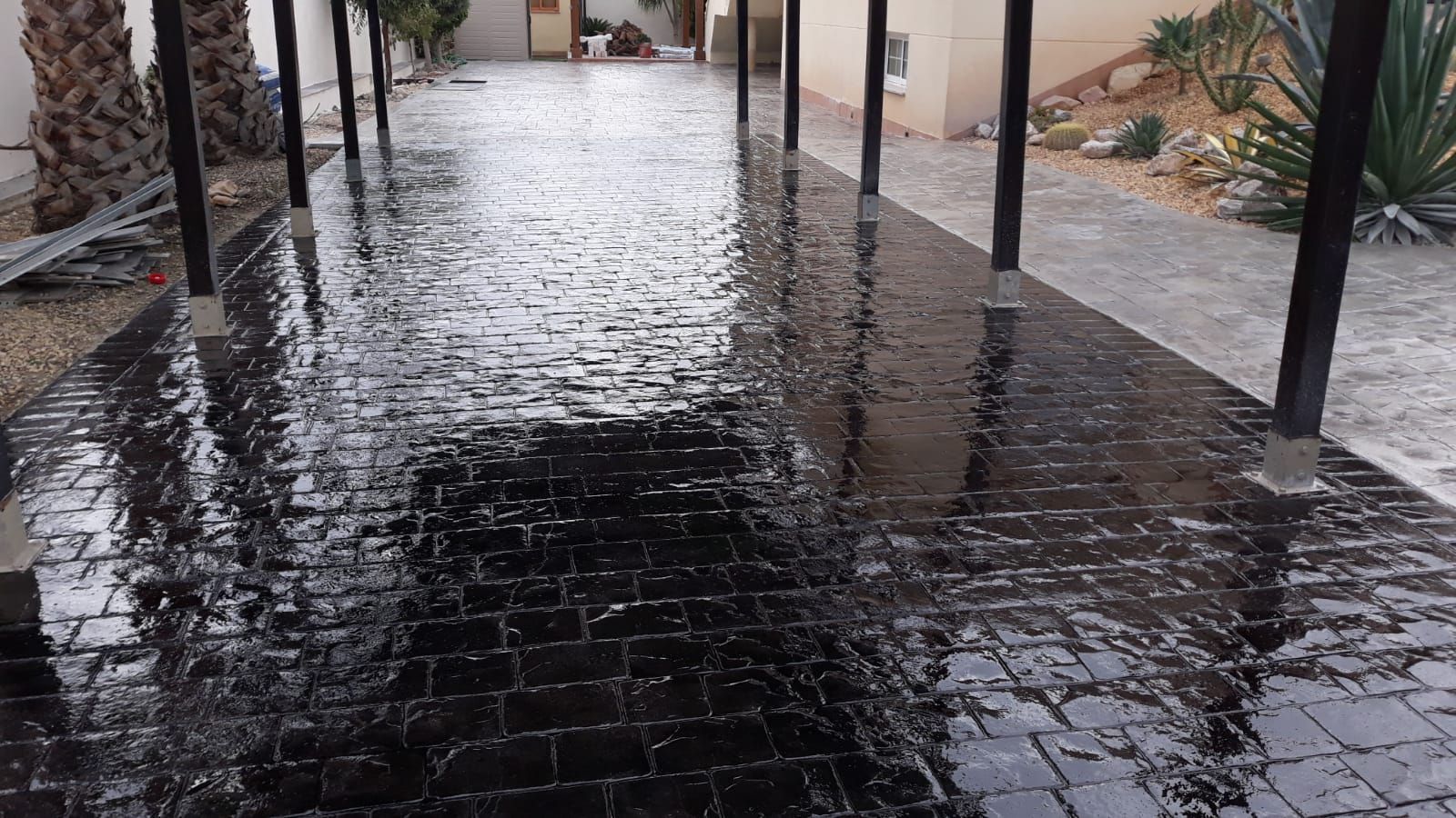 Sendero de adoquines mojados bajo un patio cubierto, que refleja la luz después de la lluvia.