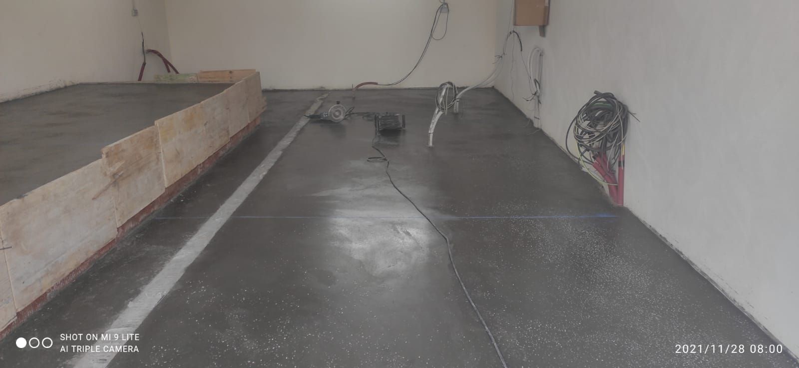 Habitación interior vacía con suelo gris, plataforma elevada a la izquierda y cables a lo largo de la pared.