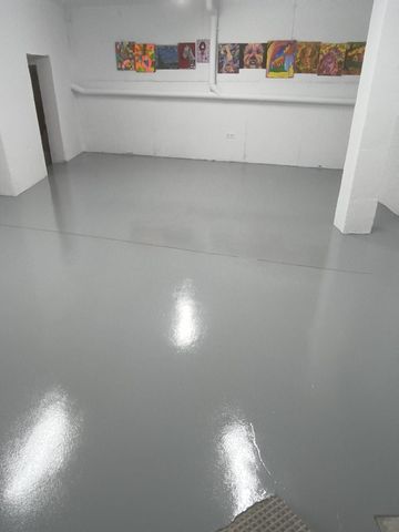 Habitación blanca vacía con suelo gris brillante y obras de arte coloridas en la pared del fondo.