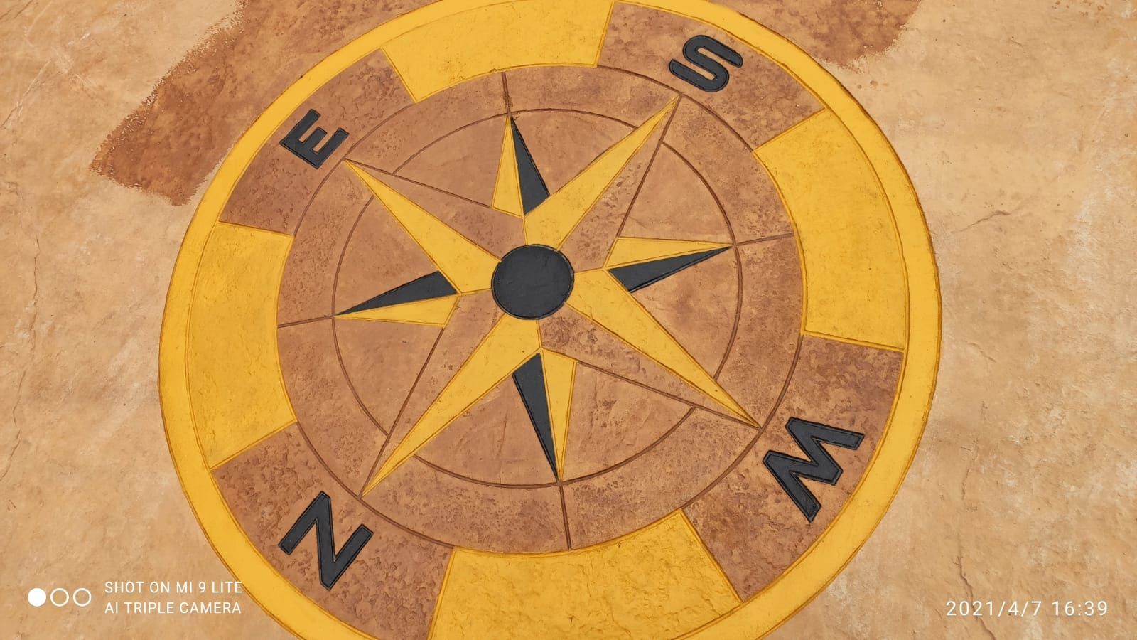 Rosa de los vientos pintada sobre un suelo de color beige, con un anillo amarillo y letras negras que indican la dirección