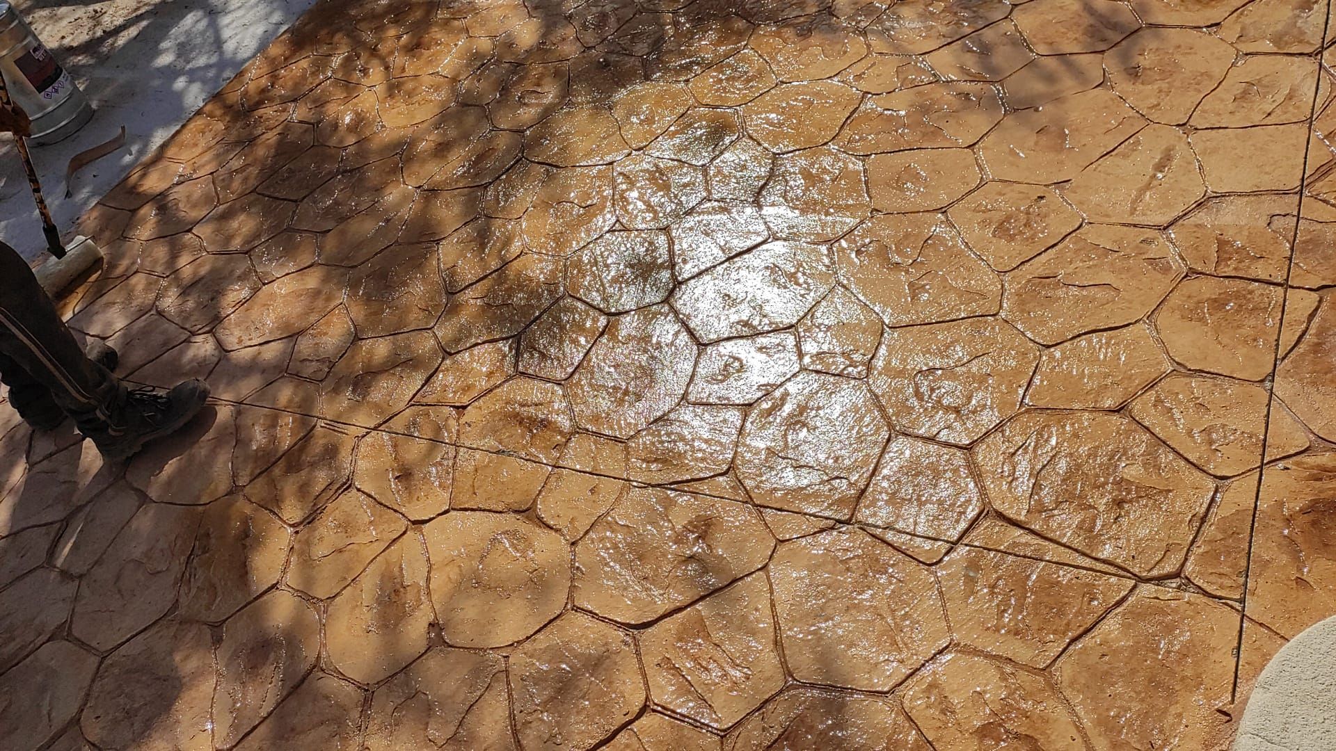 Pavimento agrietado de color marrón rojizo, iluminado por el sol, con una zona reflectante brillante