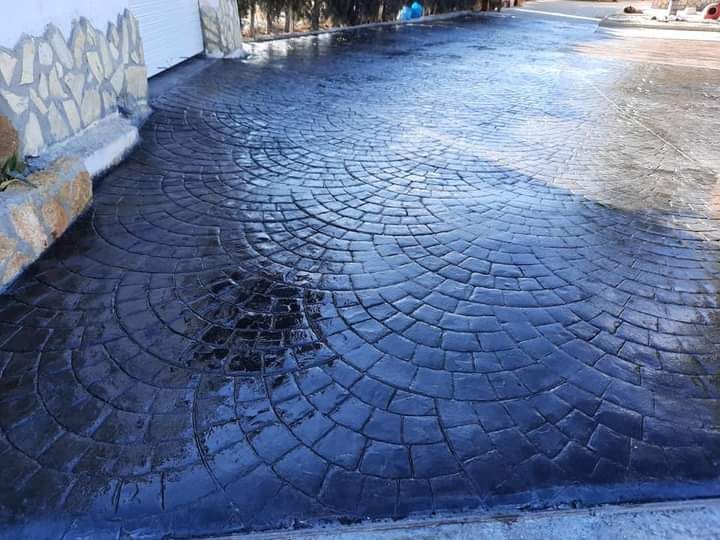 Un camino de entrada de adoquines mojados que serpentea junto a una pared blanca, reflejando la luz después de la lluvia.