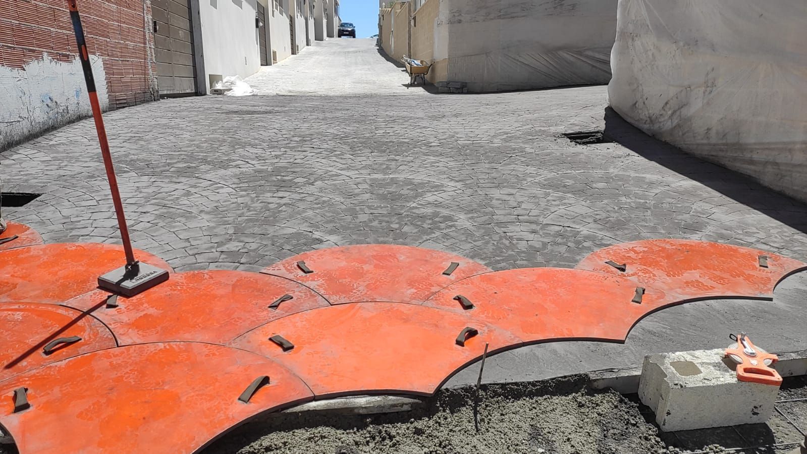 Barreras de plástico naranja bloquean un callejón de grava entre edificios.
