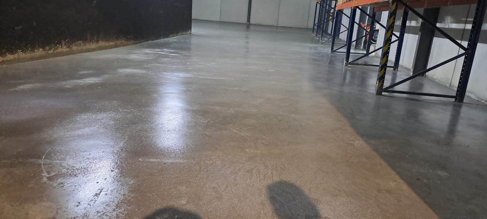Suelo de hormigón vacío en un espacio industrial con reflejos y estructuras metálicas a lo largo del lateral.
