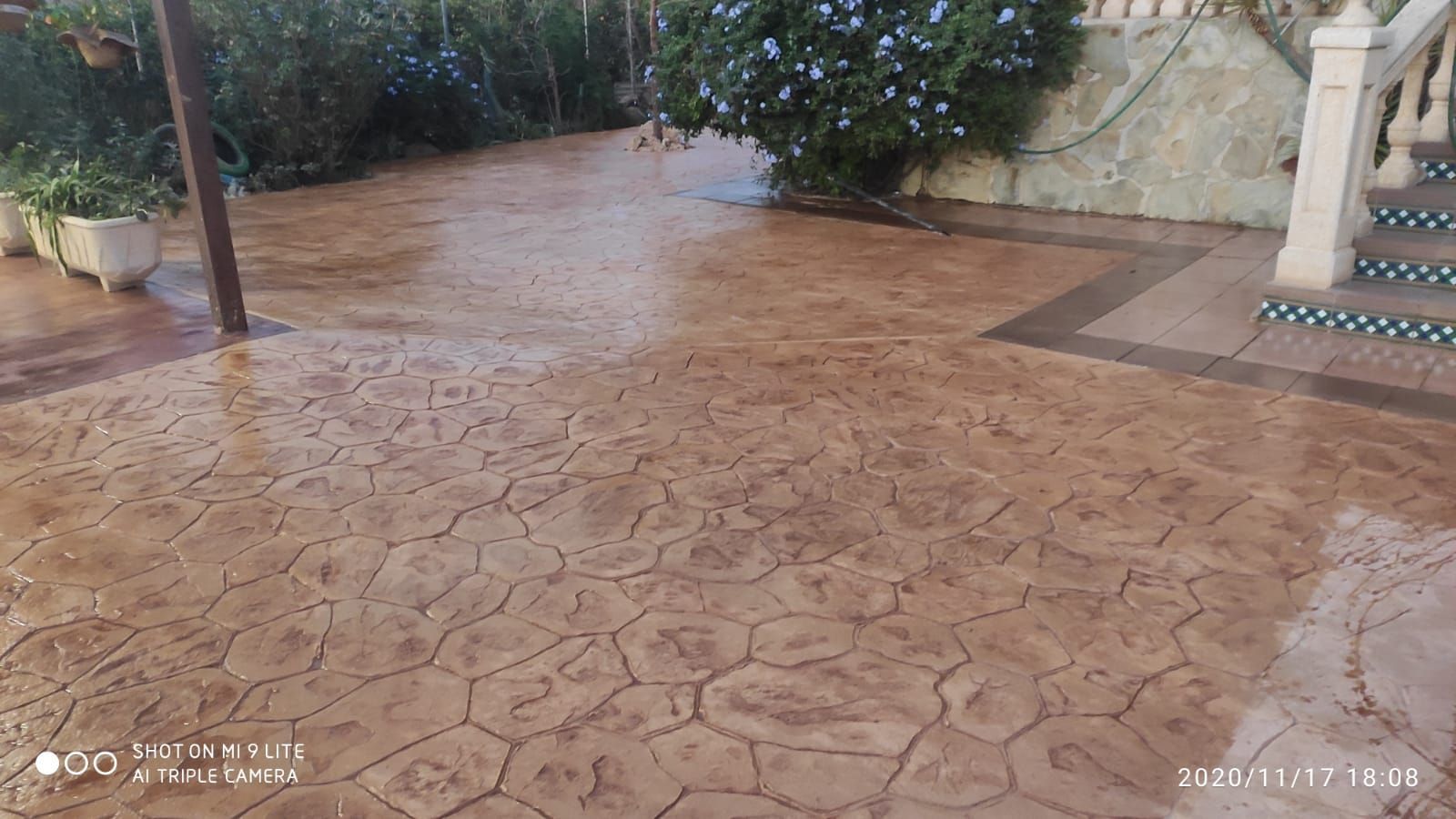 Patio de hormigón estampado húmedo en un jardín con arbustos y una escalera.