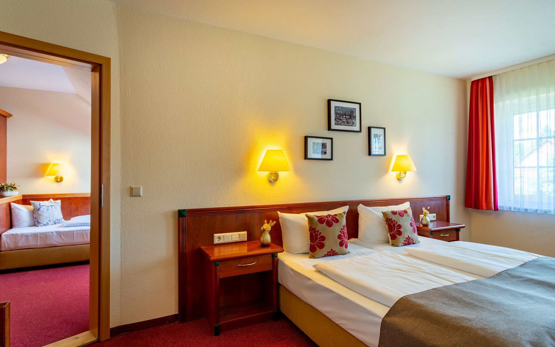 Hotelzimmer mit Doppelbett, Kunstwerken und Blick in ein weiteres Zimmer mit Schlafsofa.