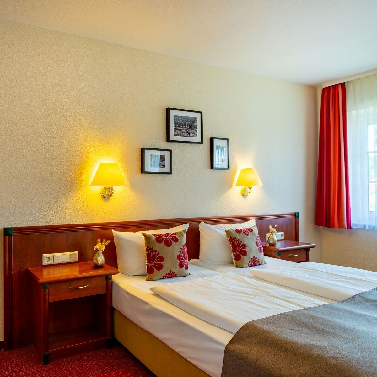 Hotelschlafzimmer mit Doppelbett, Nachttischen, Wandlampen und gerahmten Bildern.