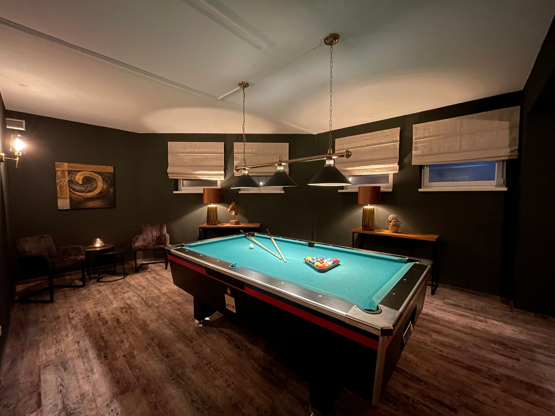 Billardzimmer mit grünem Filztisch, dunklen Wänden und warmer Beleuchtung.